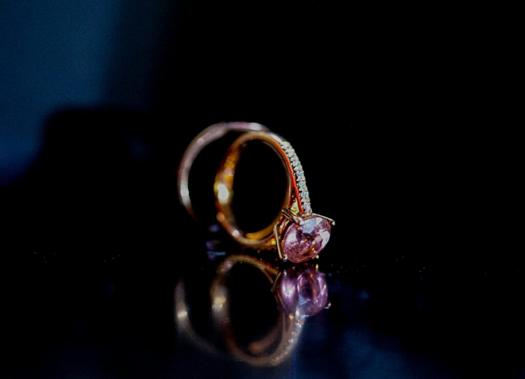 pexels-photo-2498853-2498853 Close-up of a pink gemstone ring reflecting elegantly on a dark surface, showcasing luxury and elegance.